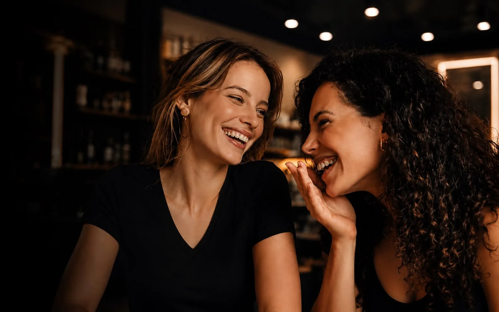 Two beauty professionals laughing together in a warmly lit salon